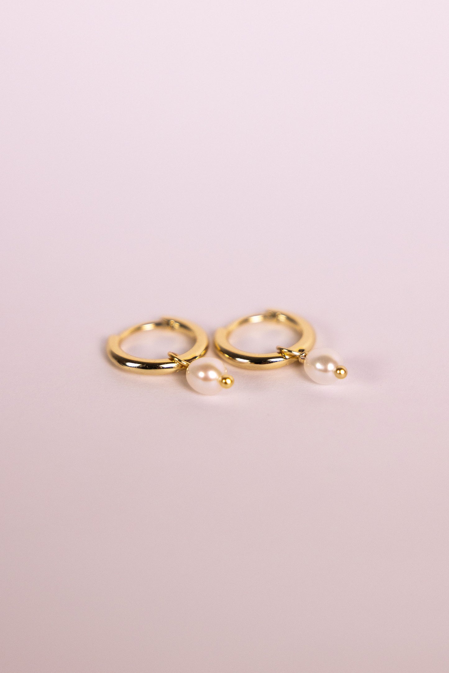 Gold hoop earrings with pearls on a neutral background