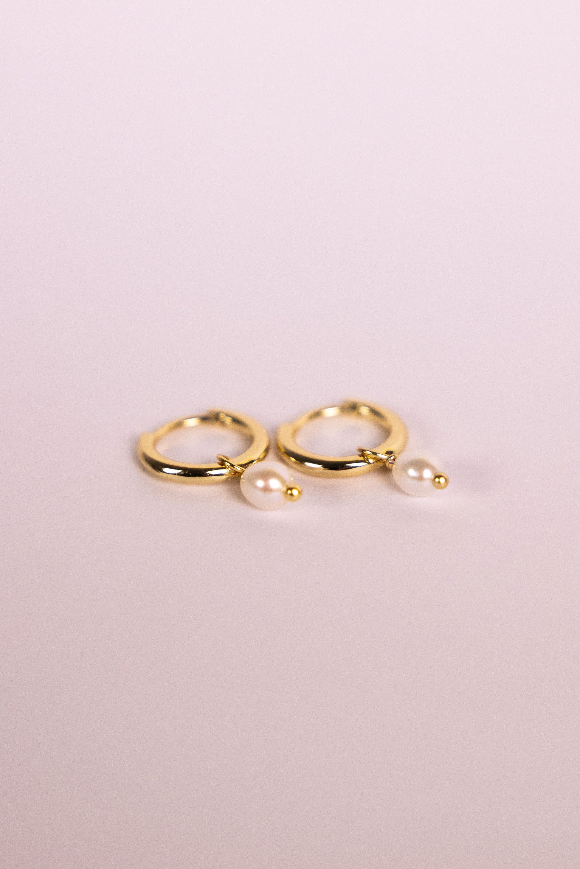 Gold hoop earrings with pearls on a neutral background