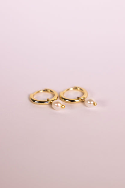 Gold hoop earrings with pearls on a neutral background