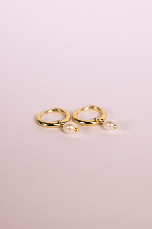 Gold hoop earrings with pearls on a neutral background