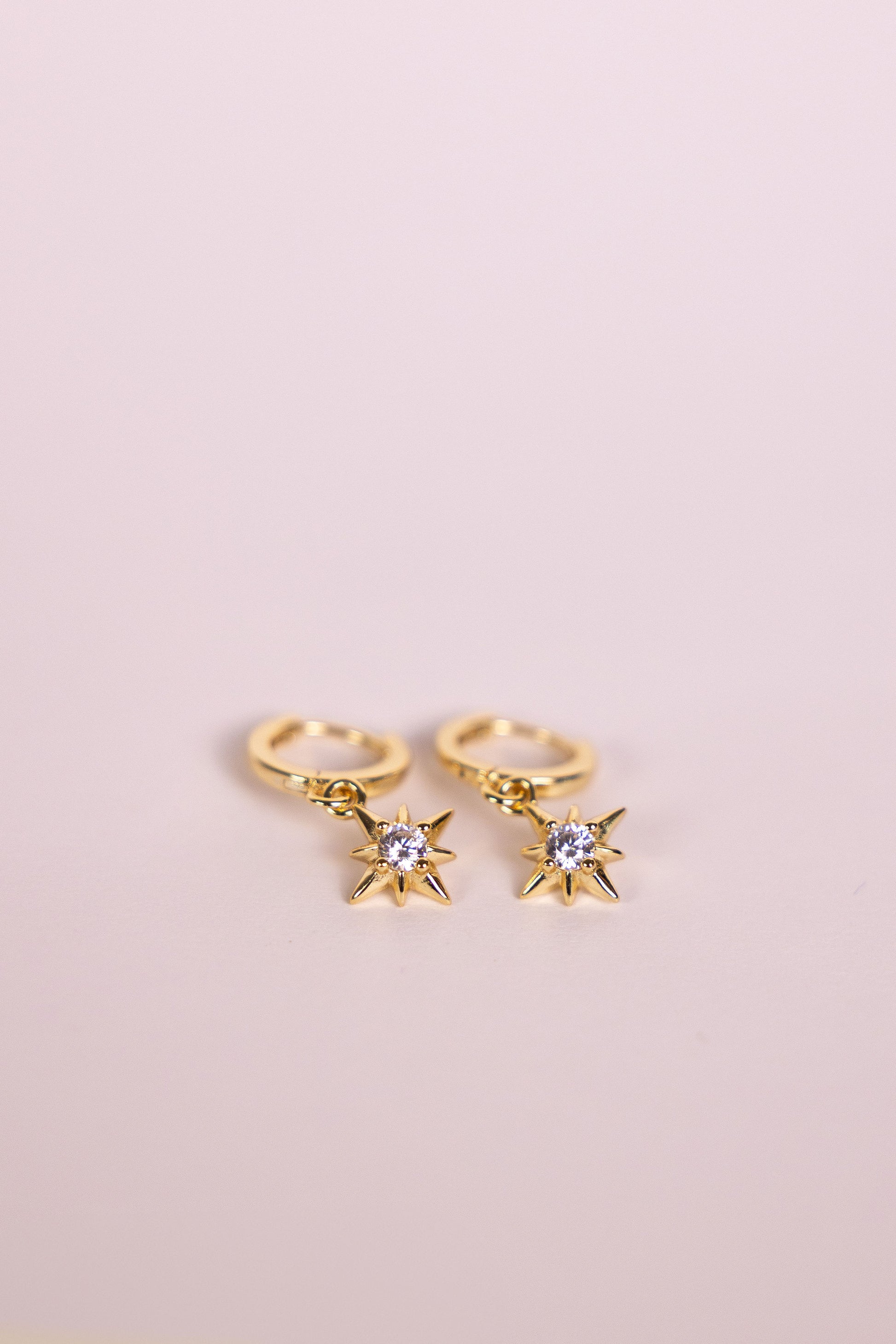 Gold hoop earrings with a star shaped charm featuring a central gemstone on a neutral background