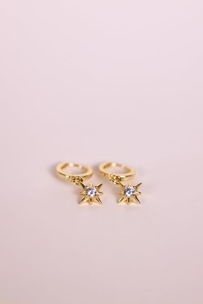Gold hoop earrings with a star shaped charm featuring a central gemstone on a neutral background