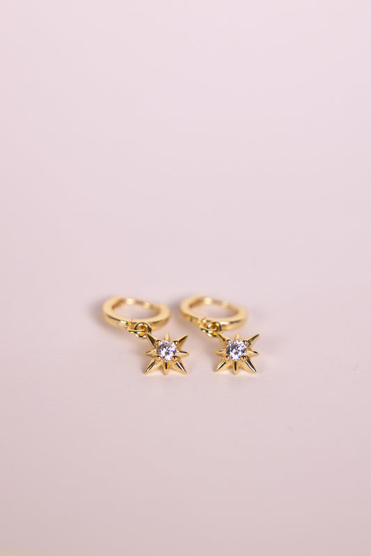 Gold hoop earrings with a star shaped charm featuring a central gemstone on a neutral background