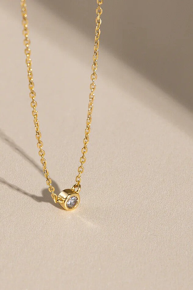 Gold necklace with a small gemstone pendant on a beige background